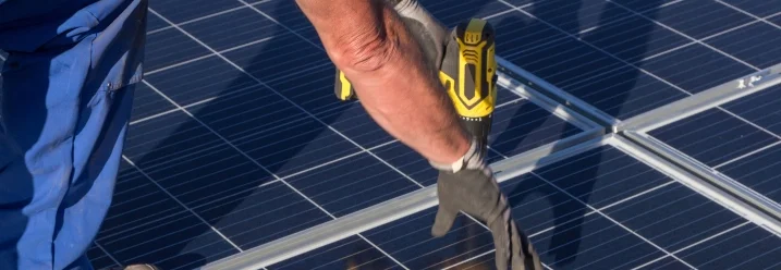 Person montiert Solarpanel mit Akkuschrauber.